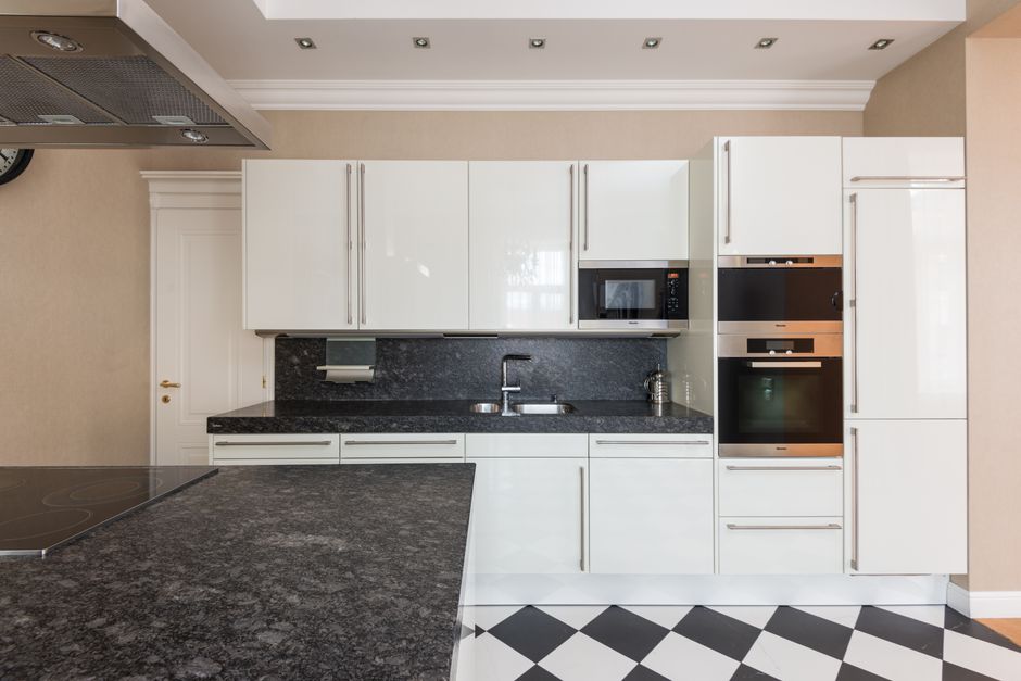 Interior design of contemporary kitchen with glossy cupboards and built in stove in marble counter under hood