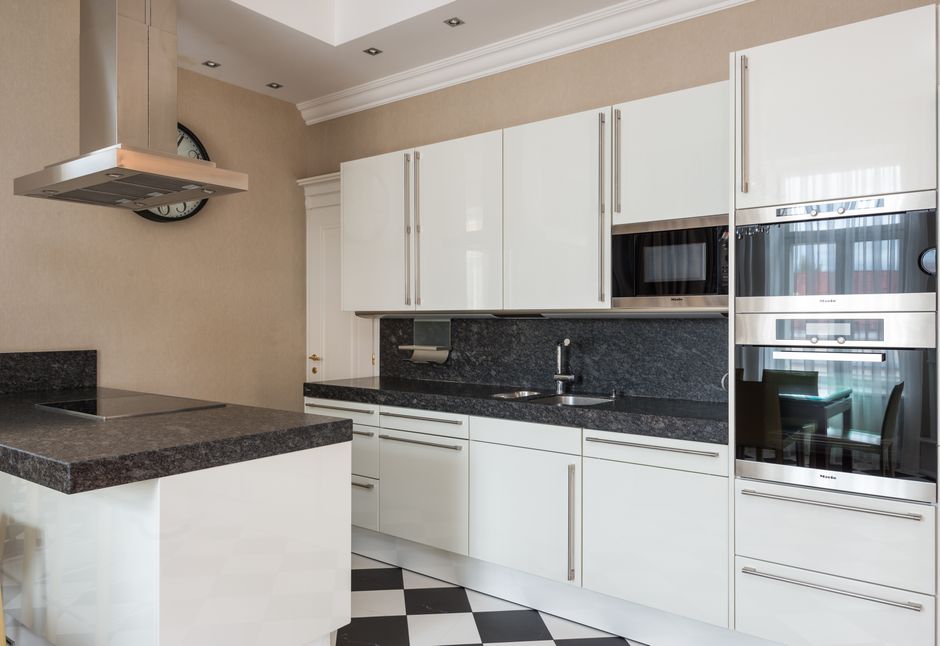 Interior of modern kitchen made in minimalist design with glossy cabinets and built in microwave oven and stove on counter under hood